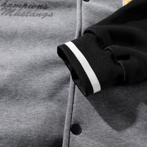 Detail of embroidered lettering and matte metal buttons on a grey knitted baseball jacket