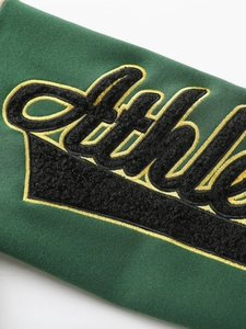 Detailed close-up of dark green sweatshirt featuring black towel embroidery and yellow stitching