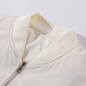 Detail von geripptem Stehkragen und silbernem Metallreißverschluss an cremeweißer Jacke
