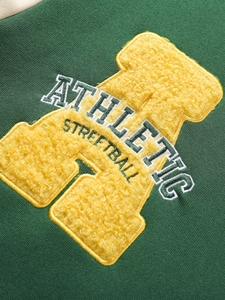 Detailed close-up of yellow chenille patch embroidery on a dark green knit sweatshirt