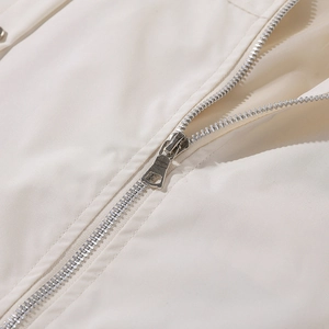Detailaufnahme eines silbernen Metallreißverschlusses an einer beigen Baseballjacke
