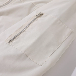 Detail von Silbermetallreißverschluss und präzisen Nähten auf cremeweißem Jackenstoff