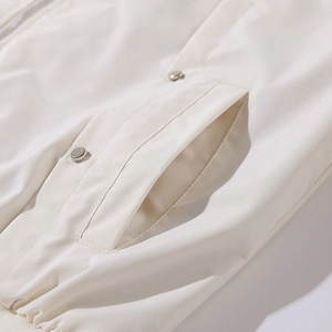 Detailansicht der Seitentasche der cremefarbenen Baseballjacke mit einem Metalldruckknopf