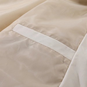 Detailaufnahme der beigen Baseballjacke mit weißem Kontraststreifen und Polyestergewebe