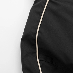Detail of black twill fabric with beige piping and precise stitching on baseball jacket