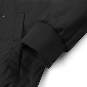 Detail der gerippten Manschette und Seitentasche mit Metalldruckknopf an schwarzer Baseballjacke