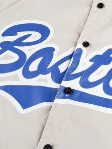 Detalle de letras azules y botón negro en una camisa deportiva de color beige