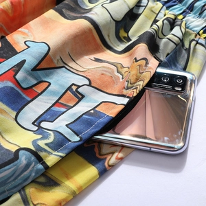 Detail showing deep side pocket of printed beach shorts with a smartphone for scale