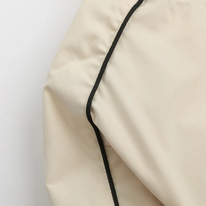 Close-up of beige woven jacket sleeve with high-density fabric and black piping detail