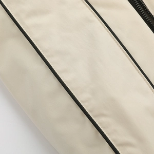 Close-up of beige jacket featuring black contrast piping and high-quality zipper detail
