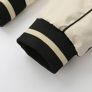 Close-up of cream baseball jacket sleeve with black ribbed cuff and white stripe detail