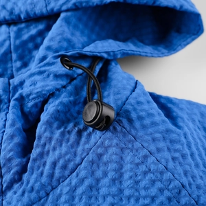 Detail of blue hooded jacket showing the windproof crinkle fabric and black drawcord toggle