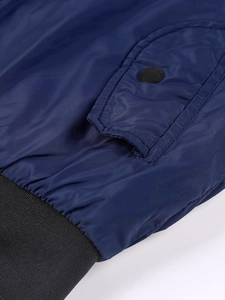Detail view of navy blue jacket featuring pocket flap with matte button and ribbed hem