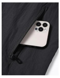 Detail of hooded windbreaker featuring functional zipper pocket with smartphone storage