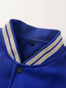 Détail du col rayé bleu et blanc et des boutons pression noirs d'une veste varsity