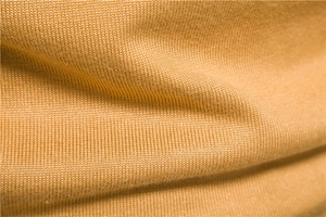 Close-up of fine ginger yellow knit fabric showing smooth texture and soft folds