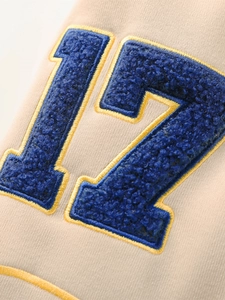 Détail du patch chenille bleu numéro 17 avec broderie jaune sur veste baseball blanche