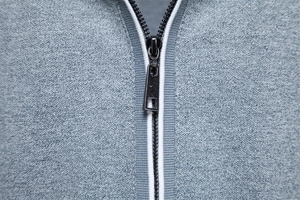 Detail of metal zipper on blue-grey knit polo shirt with white contrast trim accents