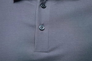Detail of dark grey polo shirt showing textured piqué fabric and two buttons on the placket