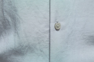 Close-up of light grey business shirt fabric texture and matte four-hole button detail
