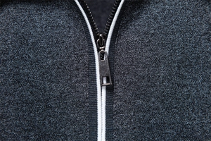 Detailed macro view of dark grey melange fabric with metal zipper and white piping accents