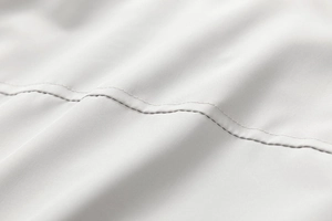 Dettaglio macro delle doppie cuciture precise su tessuto bianco per giacca premium