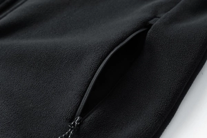 Dettaglio di una giacca in pile nero che mostra la tasca con zip e la consistenza soffice