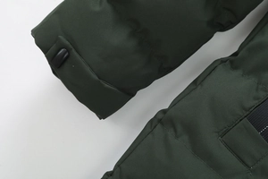 Dettaglio di cappotto imbottito verde scuro con fibbia regolabile e tessuto testurizzato