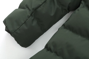 Dettaglio del tessuto trapuntato verde scuro e cuciture di precisione sul parka da uomo