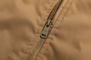 Dettaglio di una robusta cerniera in bronzo su tessuto khaki twill di una giacca
