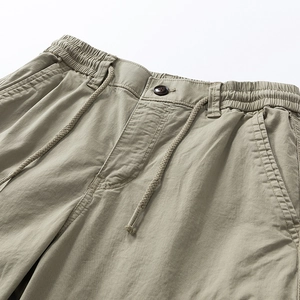 Detail of khaki cargo pants featuring elastic waist, drawstring and resin button detail