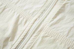 Detailed macro view of beige UPF100+ sun protection jacket with white zipper and stitching