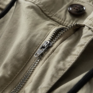 Detailed macro view of khaki cotton cargo pants featuring a YKK metal zipper and resin button