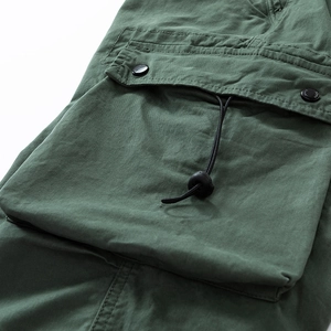 Detail of cargo pants pocket with flap, metal press studs, and elastic drawstring