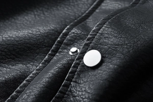 Makroaufnahme einer schwarzen Lederjacke mit Narbenstruktur und silbernen Metalldruckknöpfen