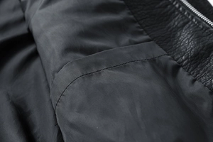 Detailaufnahme des Innenfutters der schwarzen PU-Lederjacke mit Tasche und Metallreißverschluss