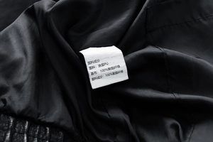 Makroaufnahme des Pflegeetiketts auf einer schwarzen PU-Lederjacke mit Materialangaben