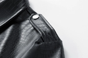 Detail of black crocodile embossed leather jacket with silver button and shoulder strap