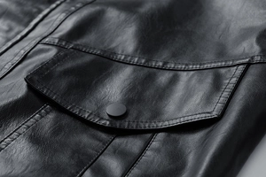 Macro shot of a black faux leather jacket pocket with matte snap button and fine stitching
