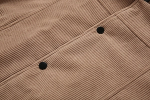 Detailaufnahme der warmbraunen Cordstruktur und schwarzen Knöpfe an der Herrenjacke