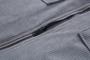 Detalle de chaqueta de pana gris mostrando cremallera metálica y textura de tela