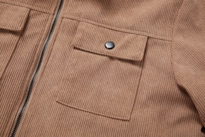 Detail einer Cordjacke in Camel mit nützlicher Tasche, schwarzem Metallknopf und Reißverschluss