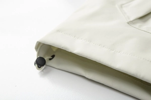 Detail des verstellbaren Saums mit schwarzem Kordelstopper an weißer Outdoorjacke