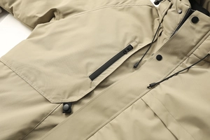 Dettaglio della giacca kaki con tasca a zip impermeabile e coulisse del cappuccio