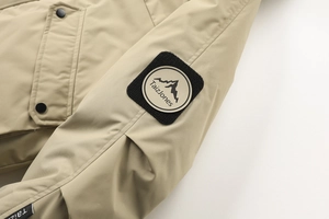 Dettaglio della manica della giacca outdoor kaki con stemma in velcro e logo della montagna