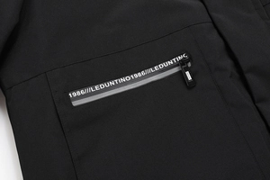 Vista macro di un parka nero che mostra la tasca con zip e scritte decorative bianche