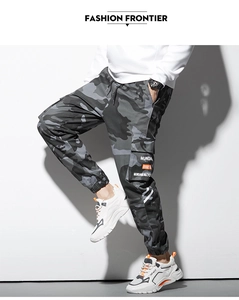 Détail du pantalon cargo avec motif camouflage noir gris et poche latérale à étiquette orange