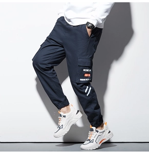 Détail de la poche cargo avec texte MUNDANE et ruban orange sur un jogging marine