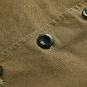 Dettaglio ravvicinato dei bottoni marrone scuro e della trama in twill di cotone kaki della giacca