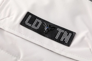 Détail d'un patch en cuir avec tête de mouton en métal et gemme bleue sur veste beige